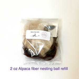 May include: A clear plastic bag containing 2 oz of alpaca fiber nesting ball refill. The fiber is a mix of light brown, beige, and dark brown colors. The bag has a label that reads "Alpaca Fiber Refill".