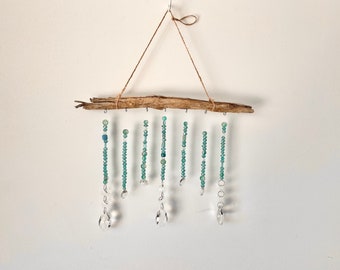 May include: A driftwood wall hanging with beaded strands and crystal drops. The beads are various shades of green and blue. The crystal drops are clear and faceted.