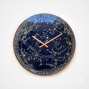 May include: A round wall clock featuring a deep blue celestial map of constellations and stars. The clock face displays white lines connecting various star clusters and labeled astronomical names. It has thin copper-colored hands and a copper frame.