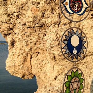 Detailed view of throat chakra, third eye chakra and heart chakra glass suncatchers. Handmade mandala glass yoga decor featuring chakra inspired symbols for meditation room styling and spiritual gifts.
