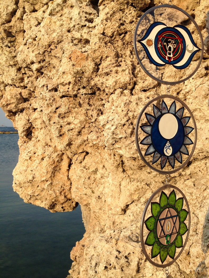 Detailed view of throat chakra, third eye chakra and heart chakra glass suncatchers. Handmade mandala glass yoga decor featuring chakra inspired symbols for meditation room styling and spiritual gifts.