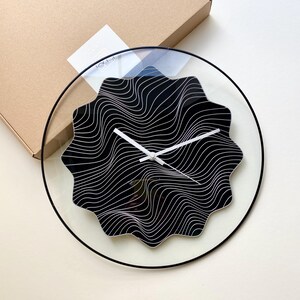 May include: A black and white abstract design wall clock with a clear glass face and a black metal frame.