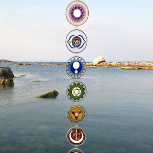 Wall hanging chakras set featuring 7 handpainted mandala glass suncatchers by Milliart Glass. Spiritual yoga decor for meditation room, chakra balancing space and meaningful gift for her. Handmade stained glass inspired chakra sun catcher set hanging beautifully near the sea.