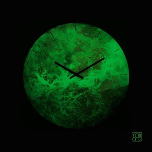 May include: A circular wall clock with a glowing green, textured surface resembling a planet or nebula. The clock features thin black hour and minute hands, simple black tick marks for the hours, and the text milli art in the bottom right corner.