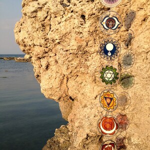 Wall hanging chakras handmade on glass featuring all seven chakra symbols. Spiritual yoga decor and chakra sun catcher set designed for meditation rooms, boho interiors and meaningful handmade gifts for her.