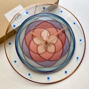 May include: A circular clock with a stained glass design featuring concentric circles in shades of pink, purple, blue, and green. The clock hands are gold and the outer rim of the clock is copper with blue dots.
