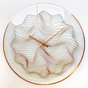May include: A modern wall clock with a white face and copper-coloured hands. The clock face features a wavy, abstract design.