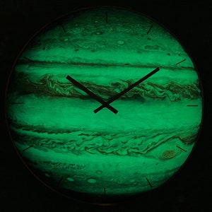 Puede incluir: Un reloj de pared redondo con un diseño verde brillante de Júpiter. La esfera del reloj presenta patrones arremolinados en tonos verdes y marrones, con manecillas y marcadores de hora negros. El reloj tiene un borde oscuro.