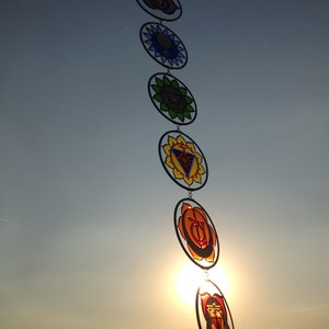 Seven chakra mandala glass suncatchers glowing beautifully in sunlight during sunset. Handmade wall hanging chakras decor for yoga room, meditation space, spiritual home styling and chakra balancing energy.