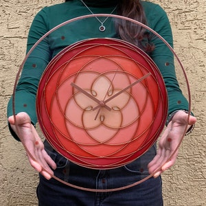 May include: A circular clock with a red, pink and orange geometric design. The clock face is surrounded by a clear glass frame.