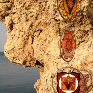 Close-up of root chakra, sacral chakra and solar plexus chakra handpainted glass suncatchers. Handmade stained glass inspired yoga decor designed for chakra balancing, meditation and spiritual interiors.
