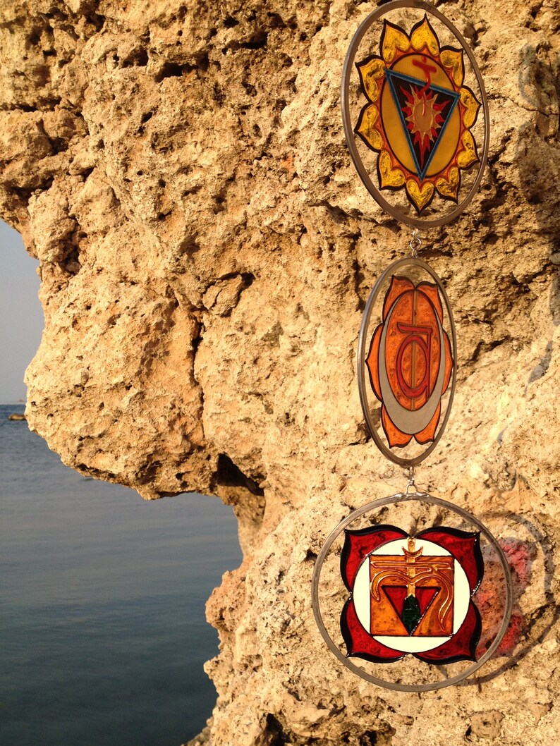 Close-up of root chakra, sacral chakra and solar plexus chakra handpainted glass suncatchers. Handmade stained glass inspired yoga decor designed for chakra balancing, meditation and spiritual interiors.