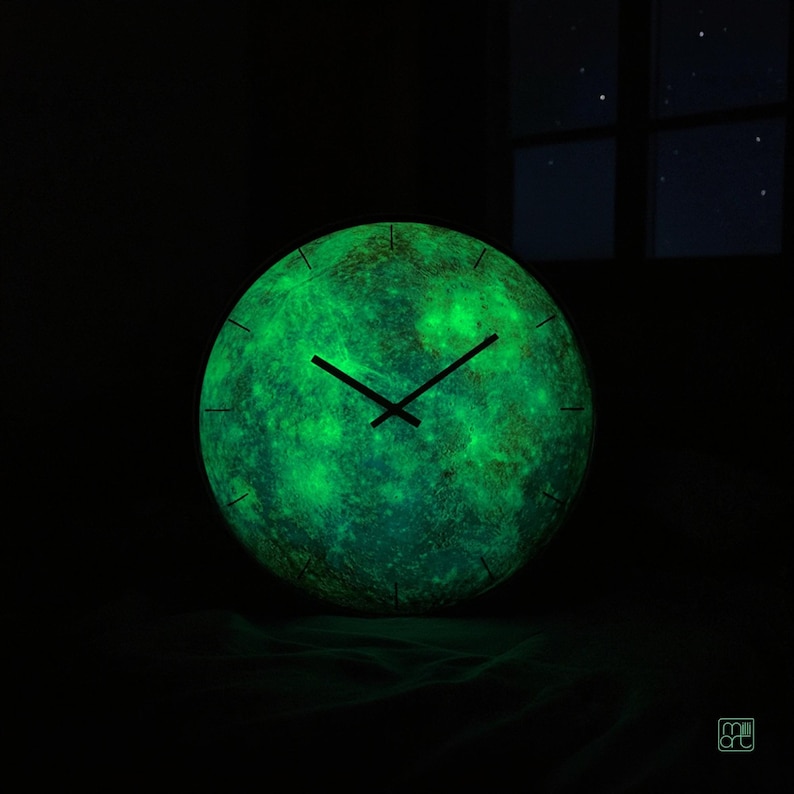 Mercury wall clock glowing green in a dark room after charging with light, showing the luminous phosphorescent details across the planetary surface.