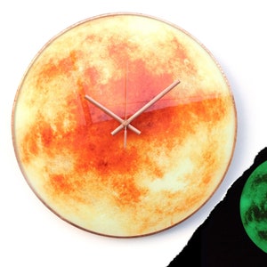 May include: A round clock with a copper-colored frame and a yellow and orange moon-like design. The clock hands are copper-colored.