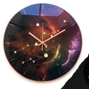 May include: A round clock with a galaxy-themed design. The clock face features a dark background with swirling nebulae in shades of red, orange, yellow, and purple. The clock hands are rose gold and the numbers are represented by small, glowing stars.
