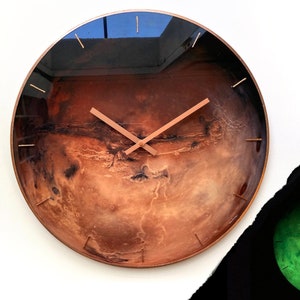 May include: A round clock with a copper-colored frame and a printed image of Mars. The clock face has a black background with copper-colored hands.
