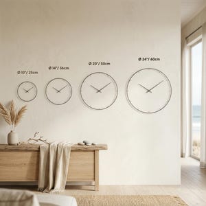 Size comparison chart showing four round wall clocks in a bright neutral interior, labeled 10"/25 cm, 14"/36 cm, 20"/50 cm and 24"/60 cm to help customers compare their scale on a wall.