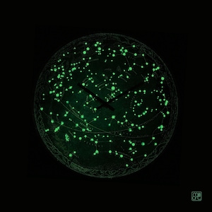 May include: A circular wall clock featuring a dark background with a glow-in-the-dark celestial star map and constellation design. The clock has two black hands positioned at the center, and the small text "mi art" is visible in the bottom right corner.
