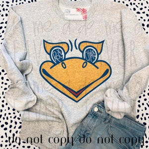 Pode incluir: Uma camisola cinzenta clara de gola redonda com um grande gráfico de uma cabeça de pássaro amarela com contornos azuis. Os olhos do pássaro contêm o texto "ROCK" e "CHALK" em letras brancas. Uma pequena etiqueta da marca é visível.
