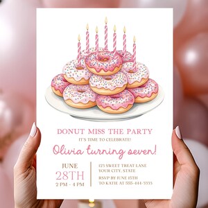 Puede incluir: Una invitación de cumpleaños con donas glaseadas rosas y velas. El texto dice "Donut Miss the Party" y "Olivia turning seven!" con detalles del evento. La invitación es sostenida por una persona.