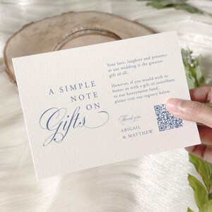 May include: A cream-colored wedding gift card with elegant blue script that reads "A Simple Note on Gifts." The card includes a QR code and text about a honeymoon fund. The card is held by a hand.