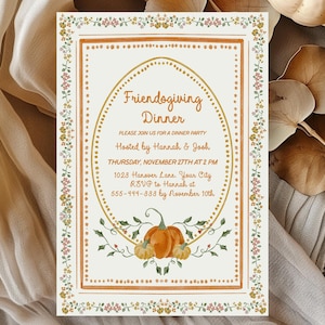 Puede incluir: Una tarjeta de invitaci&oacute;n rectangular con el texto "Friendogiving Dinner" en un marco ovalado, adornada con ilustraciones florales y de calabazas. La tarjeta est&aacute; sobre una superficie de madera con una tela blanca y una calabaza blanca. Dimensiones: aprox. 10 x 15 cm.