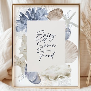 May include: A gold framed print with a watercolor design of seashells, coral, and seaweed. The print has the text "Enjoy Some Food" in a navy blue cursive font.