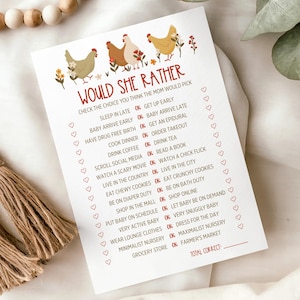 May include: A white card with the text "Would She Rather" and a list of choices for a baby shower game. The card features illustrations of chickens and floral accents. A wooden bead garland with tassels is draped nearby.