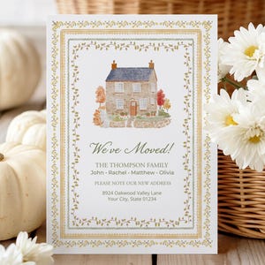 May include: A rectangular moving announcement card featuring a watercolour illustration of a stone house with a blue roof. The text reads: We've Moved! THE THOMPSON FAMILY John, Rachel, Matthew, Olivia. PLEASE NOTE OUR NEW ADDRESS 8924 Oakwood Valley Lane.