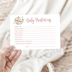 May include: A white card with pink text that says "Baby Predictions". The card has a list of predictions for a baby, including name, date of birth, time of birth, weight, height, eye color, and hair color. There is also space for the person to write "I hope you get your mom's" and "I hope you get your dad's".