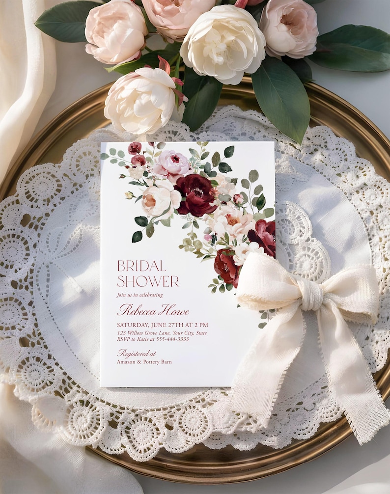 May include: A white rectangular bridal shower invitation card featuring a floral arrangement of deep burgundy and soft pink roses with green leaves. The text reads: BRIDAL SHOWER, Join us in celebrating, Rebecca Howe, SATURDAY, JUNE 27TH AT 2 PM.