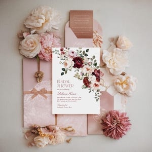 May include: A rectangular bridal shower invitation card featuring a floral arrangement of burgundy, blush, and cream flowers with green leaves. The text reads: BRIDAL SHOWER, join us in celebrating, Rebecca Howe, SATURDAY, JUNE 27TH AT 2 PM.