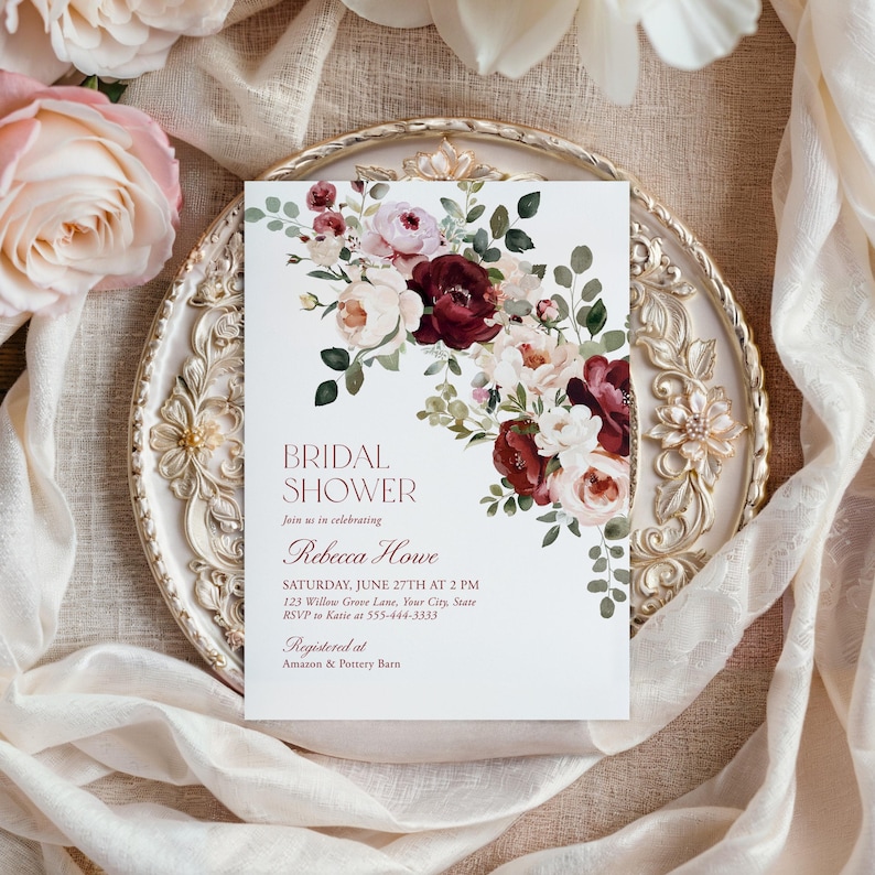 May include: A rectangular bridal shower invitation card featuring a floral arrangement of deep burgundy, blush pink, and cream flowers with green leaves. The text reads: BRIDAL SHOWER, Join us in celebrating, Rebecca Howe, SATURDAY, JUNE 27TH AT 2 PM.