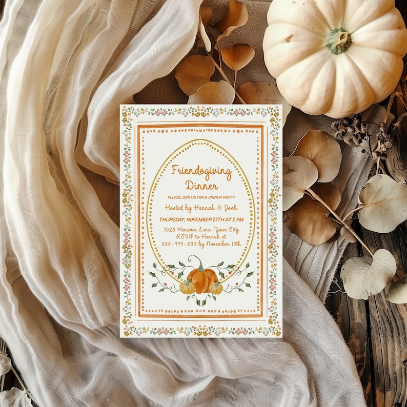 Puede incluir: Una tarjeta de invitaci&oacute;n rectangular con el texto "Friendogiving Dinner" en un marco ovalado, adornada con ilustraciones florales y de calabazas. La tarjeta est&aacute; sobre una superficie de madera con una tela blanca y una calabaza blanca. Dimensiones: aprox. 10 x 15 cm.