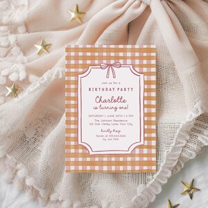 May include: A birthday party invitation with a pink and orange gingham pattern. The invitation reads "Join us for a Birthday Party, Charlotte is turning one!" with event details. The invitation is on a textured, light pink surface with gold star decorations.
