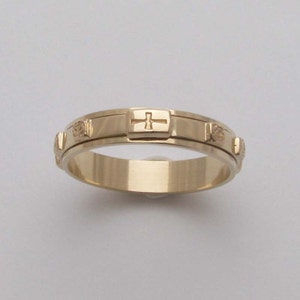 May include: A gold-coloured ring with a cross and small round details. The ring is designed to be spun around the finger.