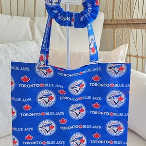 Peut inclure: Ensemble sac fourre-tout et chouchou bleus avec le logo et le texte des Blue Jays de Toronto. Le sac et le chouchou présentent un fond bleu avec le logo et le texte de l'équipe répétés sur le tissu. Un ensemble assorti.