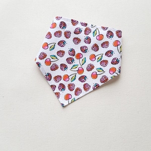May include: White bandana with a pattern of pink raspberries and red cherries. The bandana is folded in half and has a pointed tip.