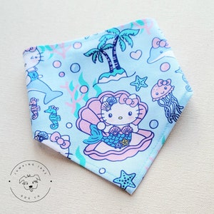 May include: A blue bandana with a white border features a repeating pattern of Hello Kitty as a mermaid in a seashell, palm trees, seahorses, starfish, and jellyfish. The bandana is made of cotton fabric.