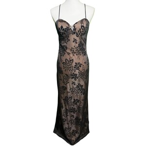 May include: A floor-length slip dress featuring a beige base layer with a black floral overlay pattern. The garment has thin spaghetti straps, a sweetheart neckline, and a small silver-toned decorative accent centered at the bust area.