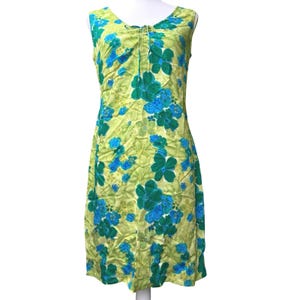 May include: A sleeveless, knee-length dress featuring a vibrant floral pattern. The dress showcases large teal and blue flowers against a light green background. It has a scoop neckline with a drawstring detail, and is made of a lightweight fabric.