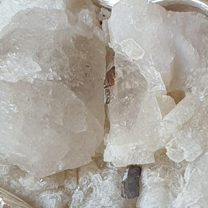 Puede incluir: Primer plano de cristales de cuarzo en bruto, transl&uacute;cidos. Los cristales tienen forma irregular con una textura rugosa y un color blanco lechoso. Algunos cristales tienen peque&ntilde;as inclusiones oscuras. Los cristales est&aacute;n dispuestos en una cesta.