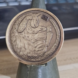 Puede incluir: Una moneda de bronce con un relieve detallado de un gato enroscado durmiendo. La moneda tiene el año MMXXXIII y la palabra "LEO" inscrita.