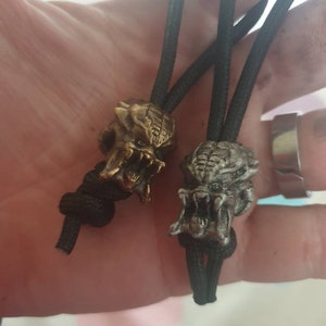 Puede incluir: Dos cordones elásticos negros con abalorios de calavera de depredador plateados y dorados. Los abalorios son detallados y tienen dientes afilados.