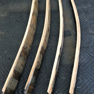 K&ouml;nnte beinhalten: Vier recycelte Holzdauben, jede mit einer gebogenen Form und verschiedenen Braun- und Graut&ouml;nen. Die Dauben sind auf einer dunklen, gesteppten Oberfl&auml;che angeordnet und zeigen die nat&uuml;rliche Holzmaserung und rustikale Textur.