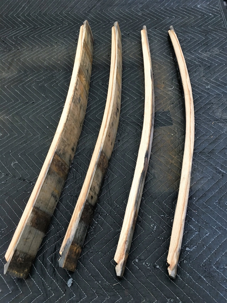 K&ouml;nnte beinhalten: Vier recycelte Holzdauben, jede mit einer gebogenen Form und verschiedenen Braun- und Graut&ouml;nen. Die Dauben sind auf einer dunklen, gesteppten Oberfl&auml;che angeordnet und zeigen die nat&uuml;rliche Holzmaserung und rustikale Textur.