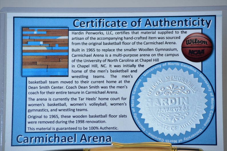 Peut inclure: Certificat d'authenticit&eacute; pour les souvenirs de Carmichael Arena. Le document comprend du texte et un logo de basket-ball Wilson NCAA. Le certificat indique que le mat&eacute;riau provient du parquet d'origine.