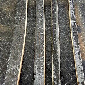 K&ouml;nnte beinhalten: F&uuml;nf recycelte Holzfassdauben mit verkohlten schwarzen Au&szlig;enseiten und abbl&auml;tternder grauer Farbe. Die Dauben sind rechteckig, mit hellen Holzkanten, und auf einer dunklen, gesteppten Oberfl&auml;che angeordnet.