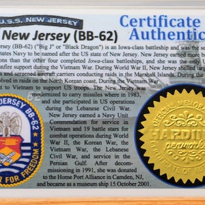 May include: A certificate of authenticity for the USS New Jersey (BB-62). The certificate includes text about the ship's history, including its service in World War II, the Korean War, and the Vietnam War. The certificate has a gold seal.