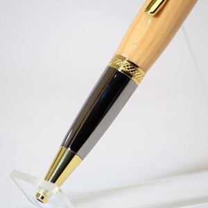 Peut inclure: Gros plan d'un stylo en bois avec des d&eacute;tails dor&eacute;s et argent&eacute;s. Le stylo pr&eacute;sente un corps en bois clair, un corps argent&eacute; et des garnitures dor&eacute;es. Il est pr&eacute;sent&eacute; sur un pr&eacute;sentoir en acrylique transparent.